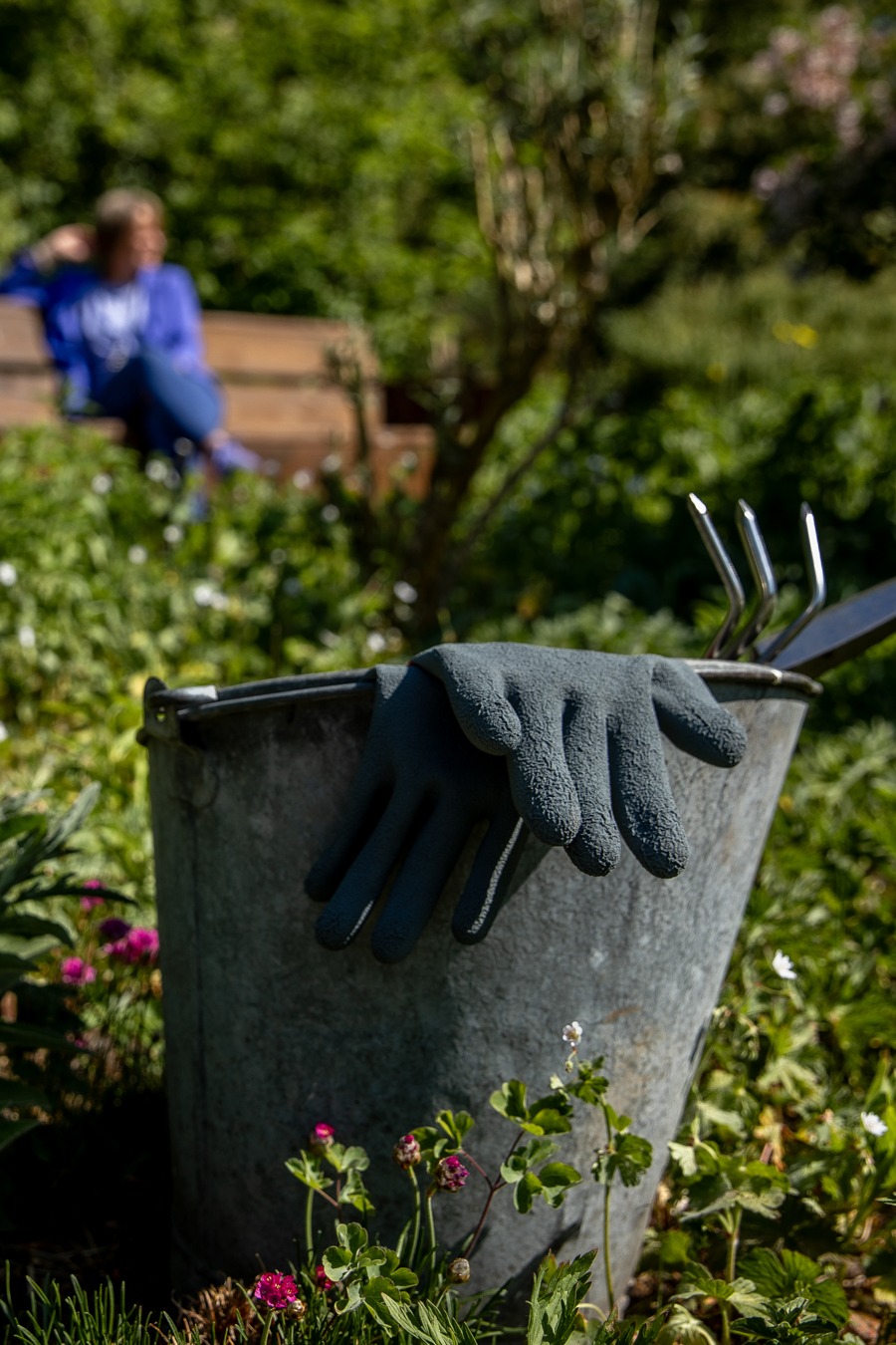 foto van emmer en tuingereedschap met op de achtergrond de ondernemerscoach op een bankje